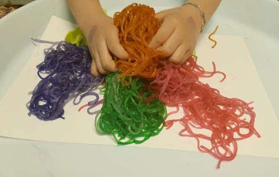 mains d'enfant jouant avec des spaghettis colorés
