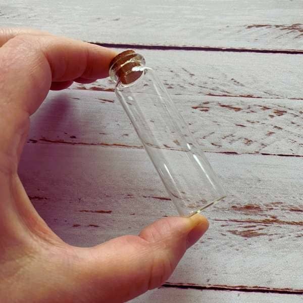 main adulte qui tient entre deux doigts la fiole éprouvette en verre avec un bouchon de liege.